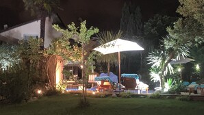 Área externa com mesas e cadeiras para relaxar à noite, incluindo guarda-sóis e uma pequena mesa.