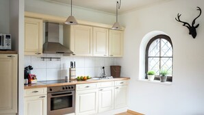 A kitchen with white cabinets, a stove, and a microwave. There is a window with plants on the windowsill. - Das Nordberg Apartments (Garmisch-Partenkirchen)