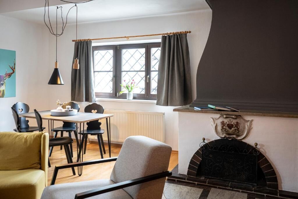 A cozy living room with a fireplace, a dining table with chairs, and a window with curtains.