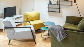 A modern living room with wooden beams, a skylight, a flat-screen TV, a yellow sofa, a green sofa, and a small table. - Das Nordberg Apartments (Garmisch-Partenkirchen)