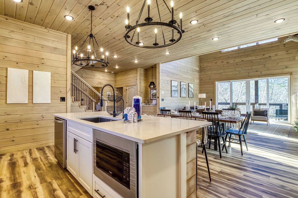 A spacious kitchen with a central island, wooden walls, and a chandelier.