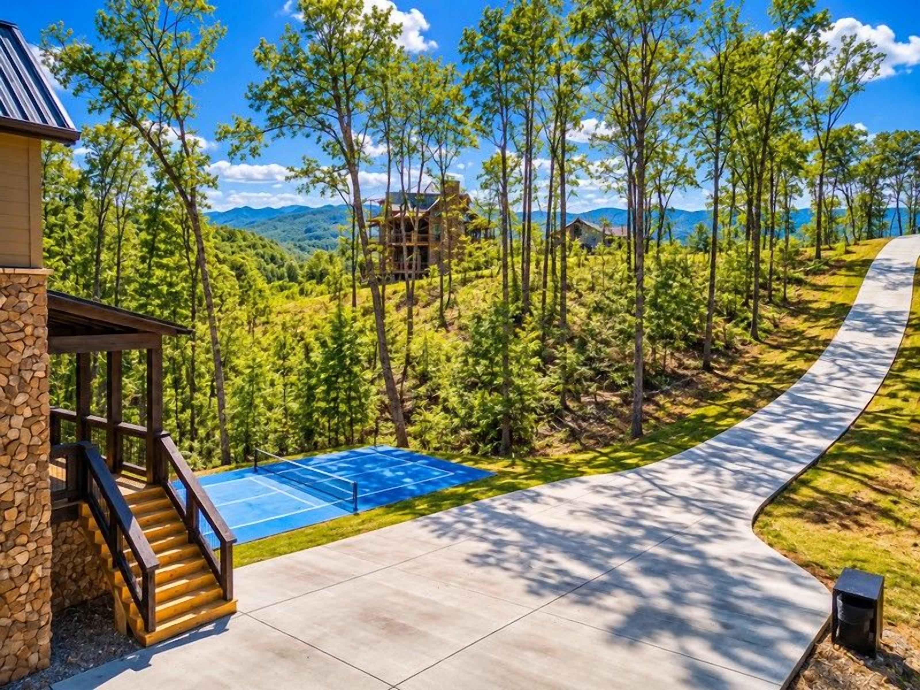 A residential property with a paved driveway, a tennis court, and a stone building with a wooden staircase.