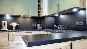 A modern kitchen with light green cabinets, a black countertop, and stainless steel appliances.