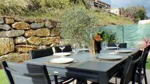 An outdoor dining area with stone walls, a table set for four, and a view of a hillside with buildings.