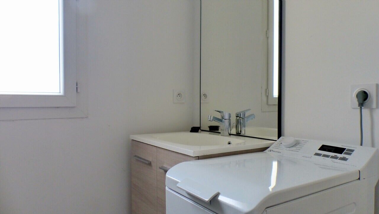 A compact laundry room with a washing machine, a sink, and a mirror.