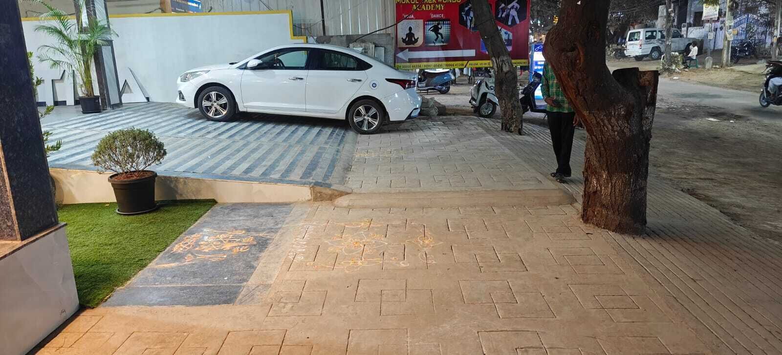 A white car parked in front of a building with a paved entrance and a small tree.