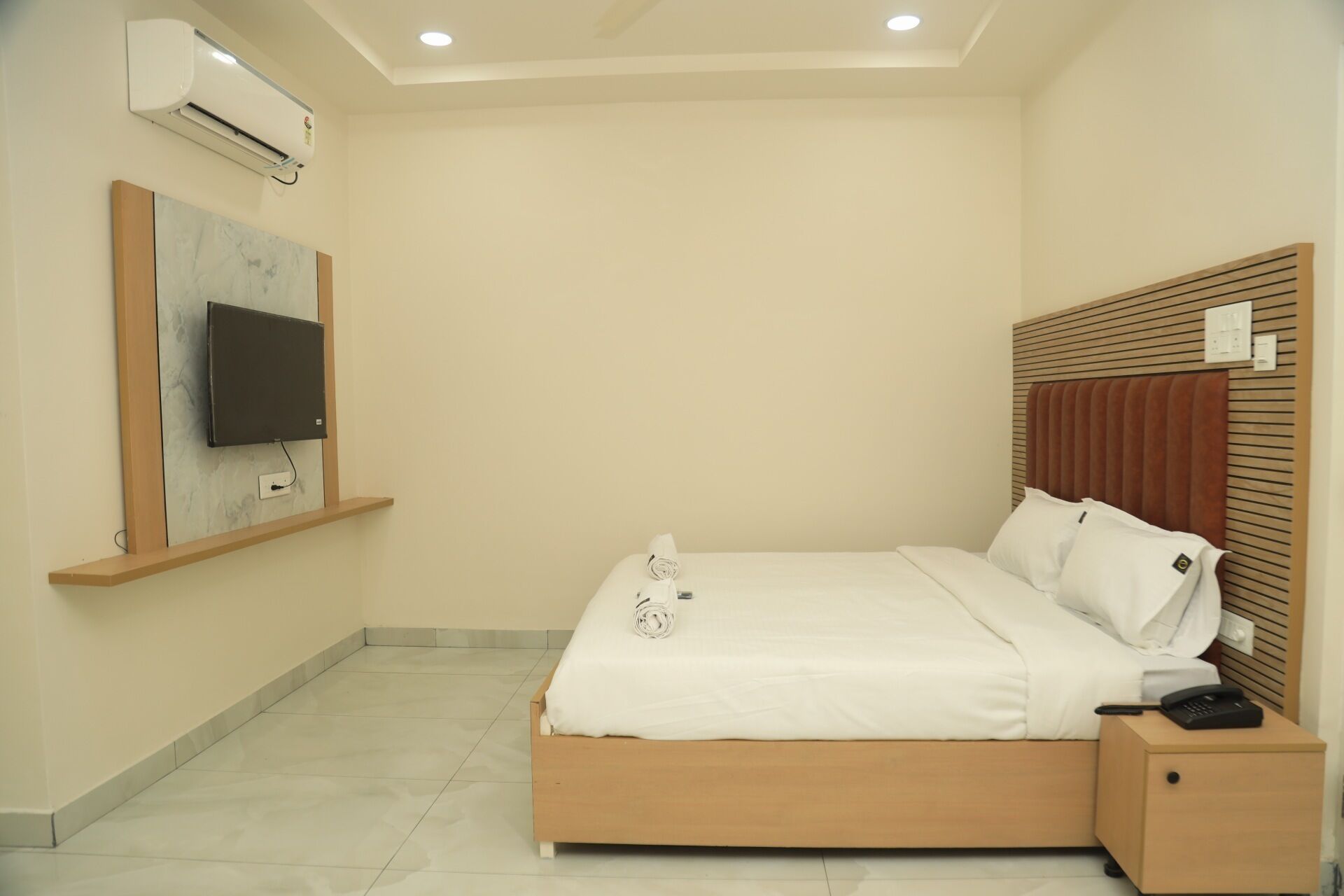 A neatly arranged bedroom with a bed, bedside table, and a mounted TV.