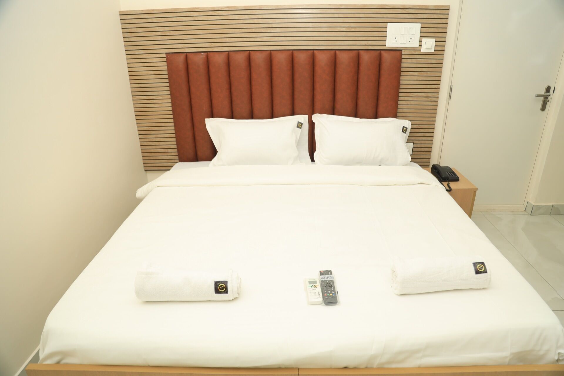 Un letto rifatto con lenzuola bianche, una testiera in legno e un comodino con un telefono.
