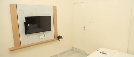 A hotel room with a flat-screen TV mounted on a marble wall, a bedside table with a remote control, and a white bed.
