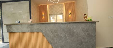 A reception desk with a marble top, wooden paneling, and a modern ceiling design.