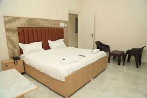 A hotel room with a large bed, a bedside table, a chair, and a small table. - Varrahi Exotica  (Hyderabad)