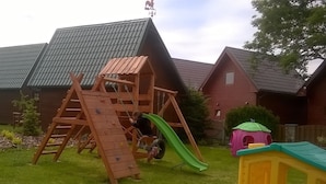 A wooden play structure with a slide and climbing ladder in a backyard with houses in the background. - Agroturystyka Pod Jesionem  (Wladyslawowo)