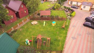 Enjoy a family-friendly backyard with a swing set, slide, and playhouse, surrounded by a garden and mature trees.