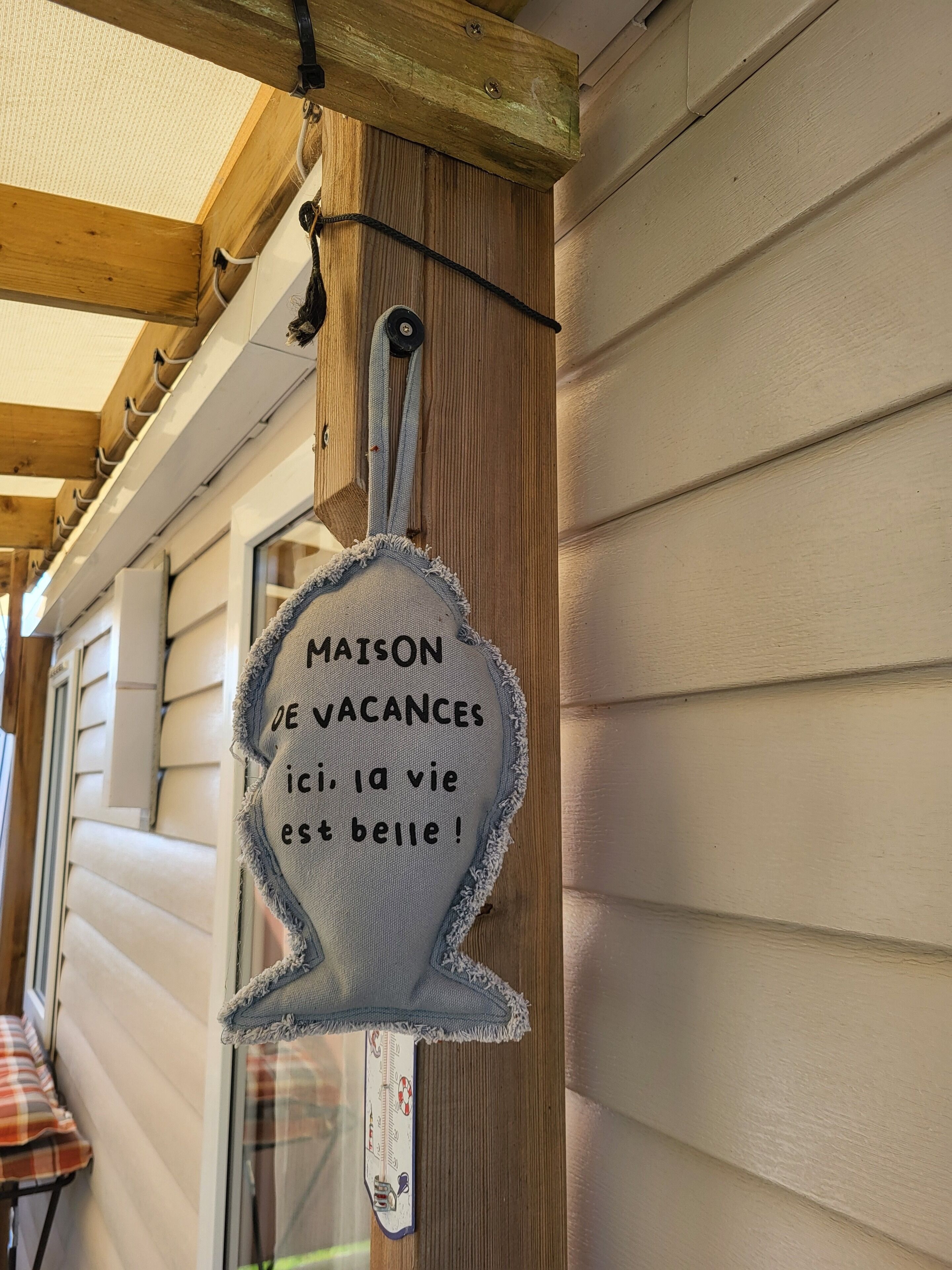 A wooden exterior wall with a hanging sign that reads 'MAISON DE VACANCES ici, la vie est belle!'