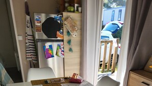 A compact dining area with a table set for two, a refrigerator, and a wooden cabinet. - La bretagne ça gagne vous!! near Vannes Sarzeau STgildas de ruys (Surzur)