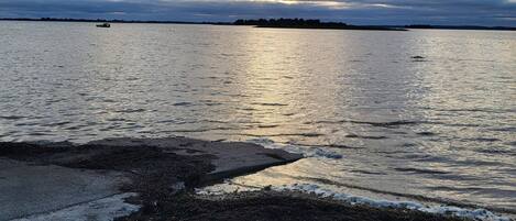 A coastal scene with a rocky shoreline, calm water, and a distant landmass under a cloudy sky.