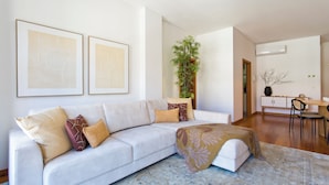 A modern living room with a sofa, a dining table, and a large plant. - Boutique Rentals-SãO*bEnTo Ribeira Apt (Porto)