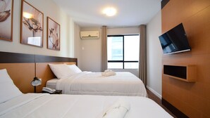 A hotel room with two beds, a TV mounted on the wall, and a window with curtains.