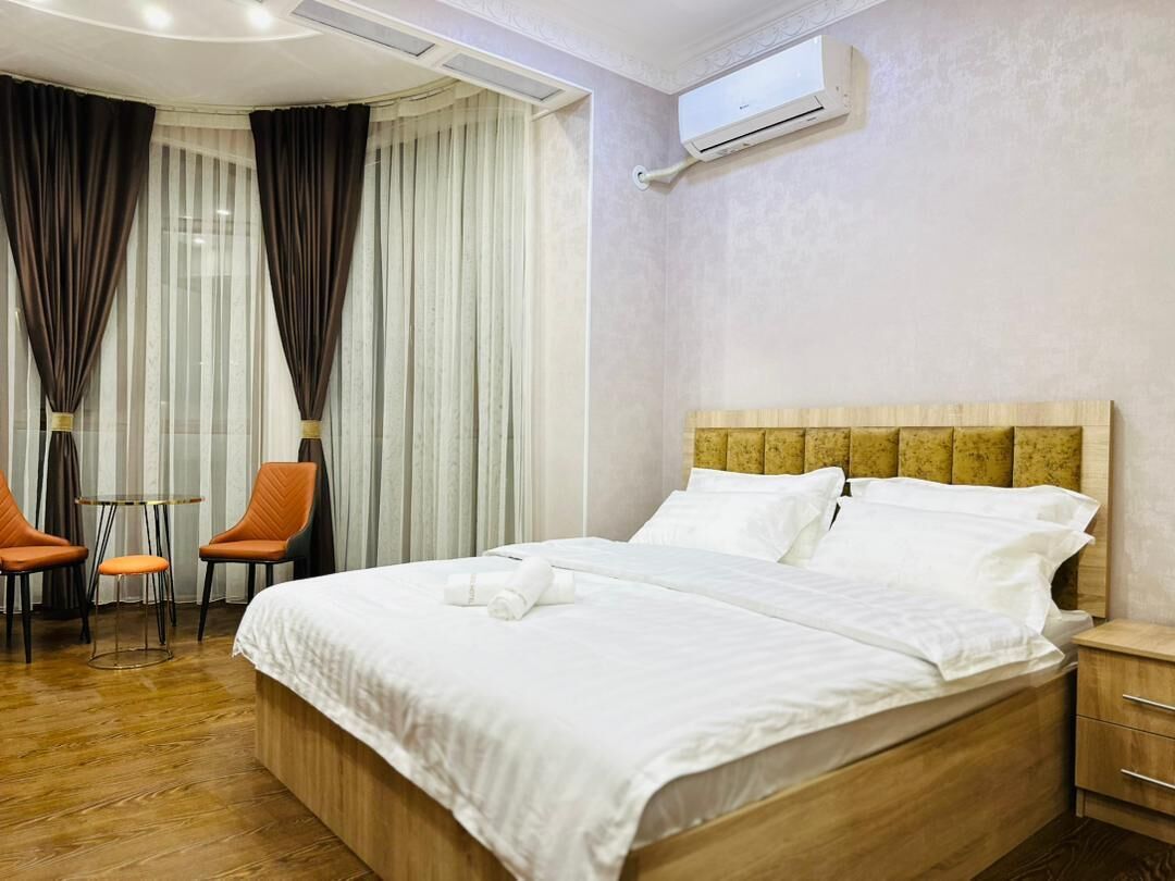 A hotel room with a wooden bed, white linens, a small table with two chairs, and an air conditioning unit on the wall.