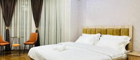 A hotel room with a wooden bed, white linens, a small table with two chairs, and an air conditioning unit on the wall.