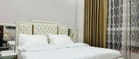 A neatly arranged hotel room with a large bed, a bedside table, a chair, and a mirror.