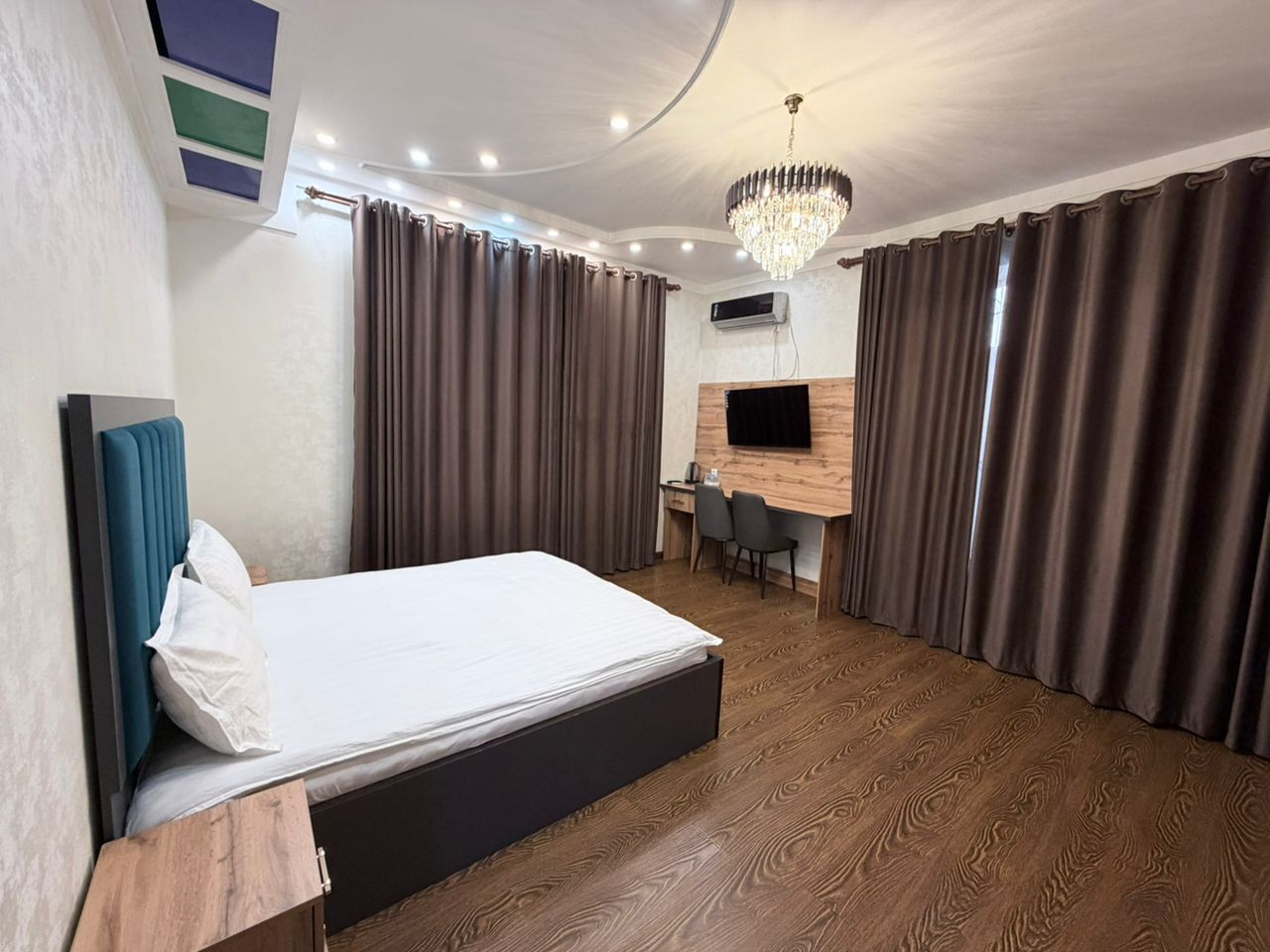 A hotel room with a bed, a desk, a chair, a TV, and a chandelier.