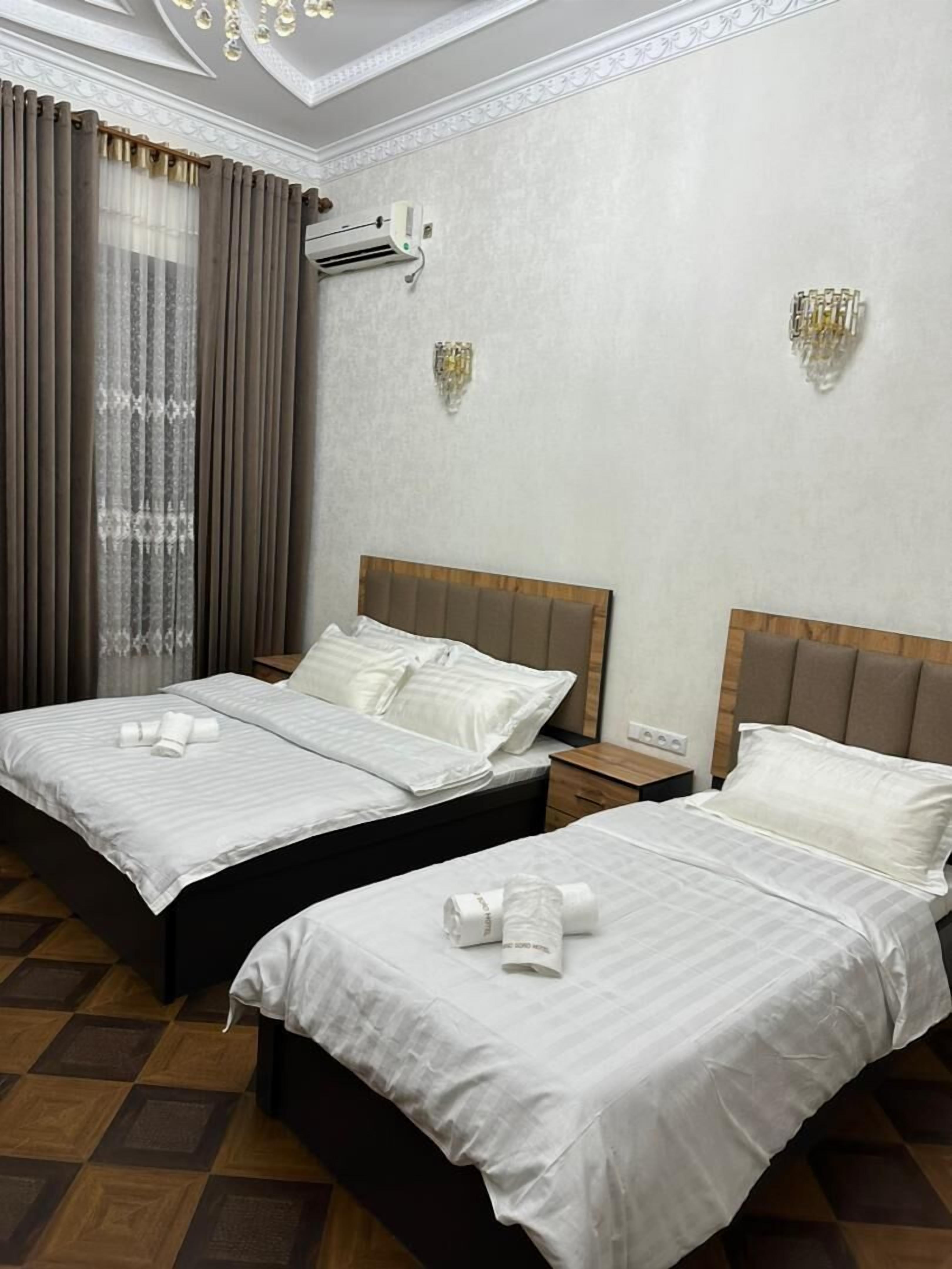 Ett hotellrum med två sängar, ett stort fönster med gardiner, en luftkonditioneringsanläggning och dekorativa vägglampor.