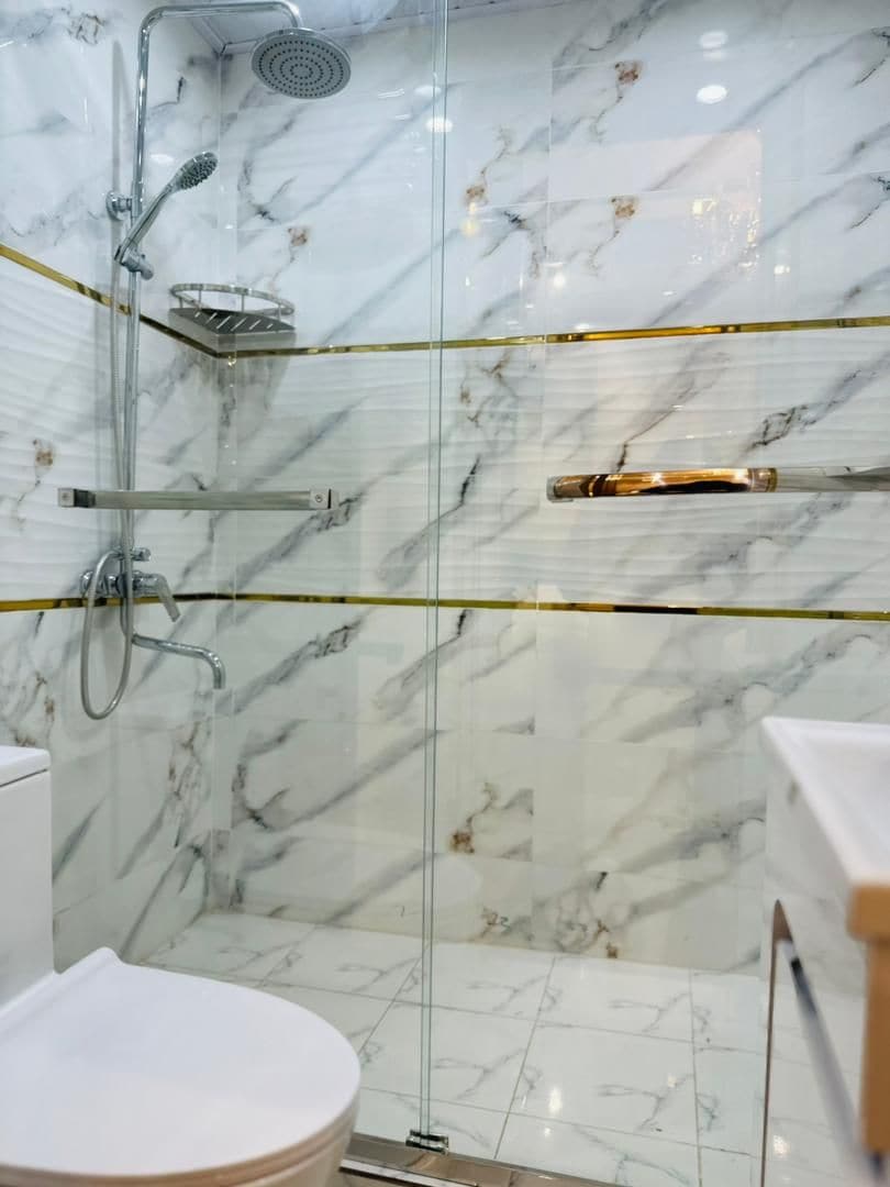 A bathroom with a glass-enclosed shower, marble walls, and a toilet.