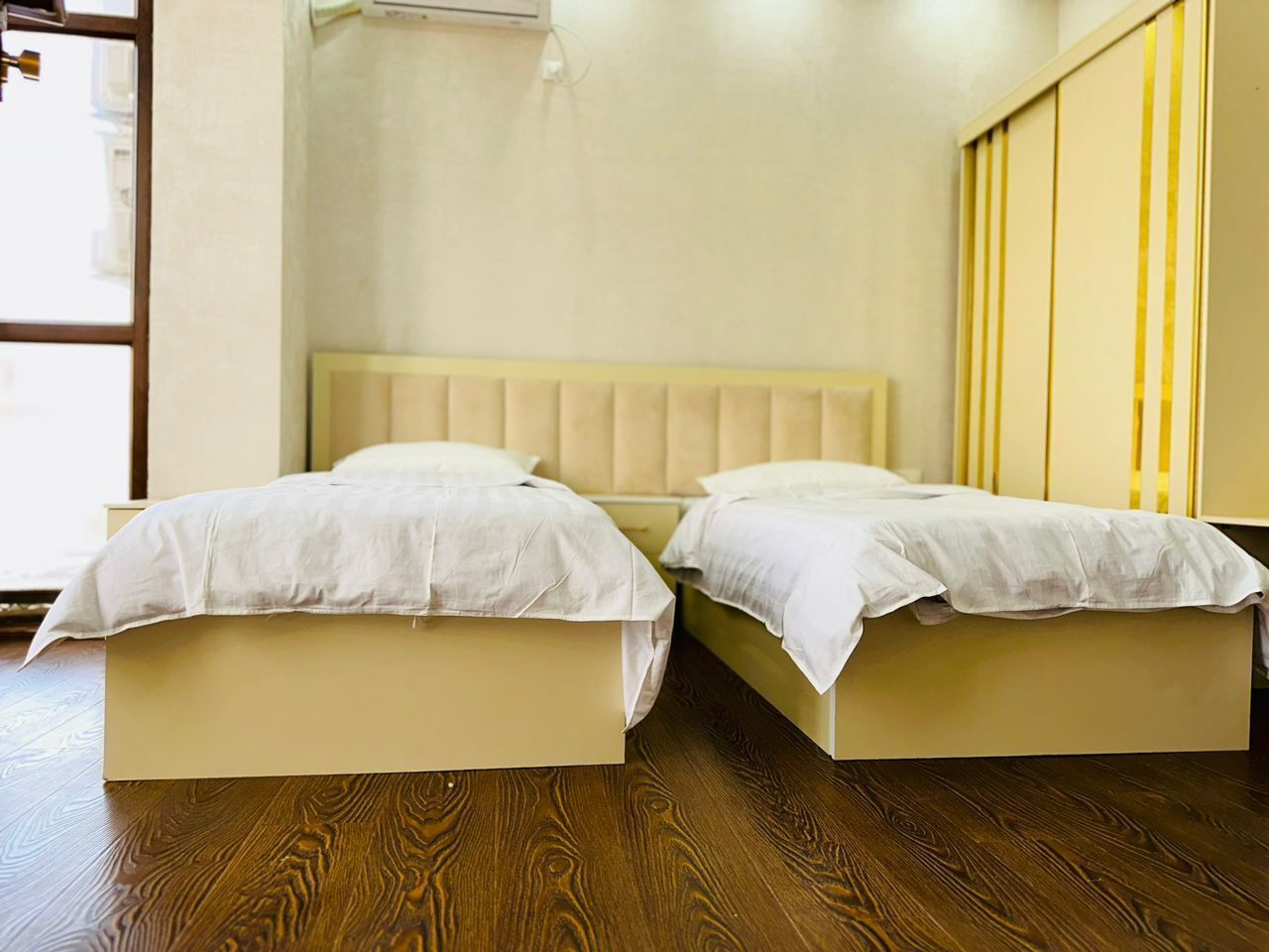 A room with two beds, a wooden floor, and a beige headboard.