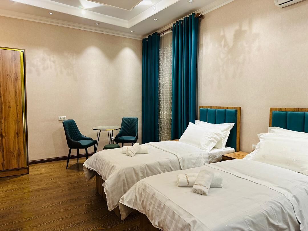 Habitación de hotel con dos camas, una mesita, dos sillas y una puerta de madera.