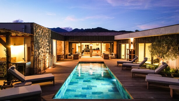 Une piscine avec des chaises longues, un mur en pierre et une vue sur les montagnes en arrière-plan.