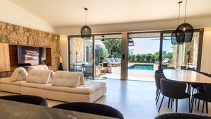 Un salon moderne avec un mur en pierre, un téléviseur à écran plat, un canapé et un coin repas comprenant des chaises et une table.