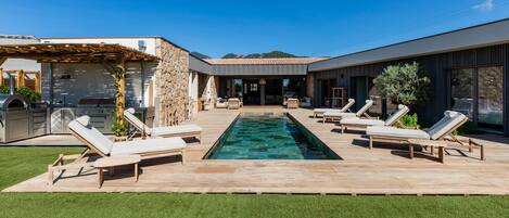 Un área de piscina moderna al aire libre con sillones reclinables y una pared de piedra.