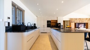 Une cuisine moderne avec des meubles blancs, un îlot central et une cheminée en pierre.