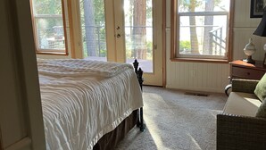 A bedroom with a large bed, a chair, and a view of the outdoors through a door. - Beautiful Lake Front Home on Lake Almanor. (Westwood)