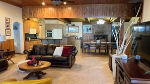 A spacious living room with a leather sofa, a yellow ottoman, and a dining area with a wooden table and chairs. - Beautiful Lake Front Home on Lake Almanor. (Westwood)