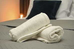 A neatly folded white towel on a bed with a textured grey bedspread. - Warrington Suites by Relax Stays (Warrington)
