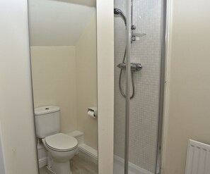 A small, enclosed bathroom with a toilet, a shower enclosure, and a toilet paper holder. - Warrington Suites by Relax Stays (Warrington)