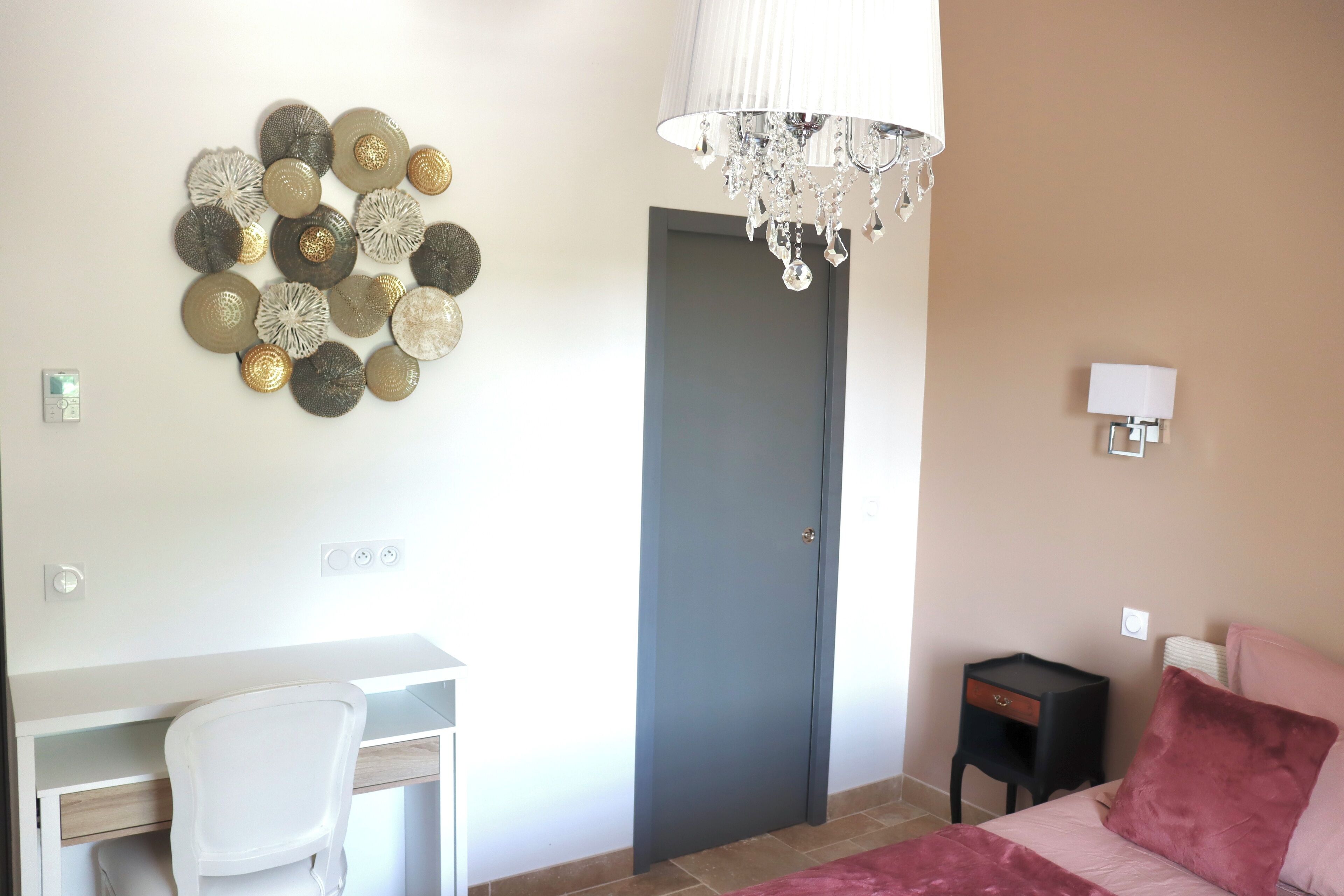 Een slaapkamer met een bed, bureau, stoel, een kroonluchter en een decoratie aan de muur.