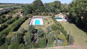 Vista aérea de una propiedad con piscina rectangular rodeada de césped cuidado y varios árboles.