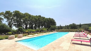 Una piscina rectangular con solárium alicatado, rodeada de sillas de descanso color beige y una valla metálica.