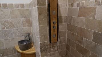 A small, tiled shower area with a wooden bench and a bowl sink.