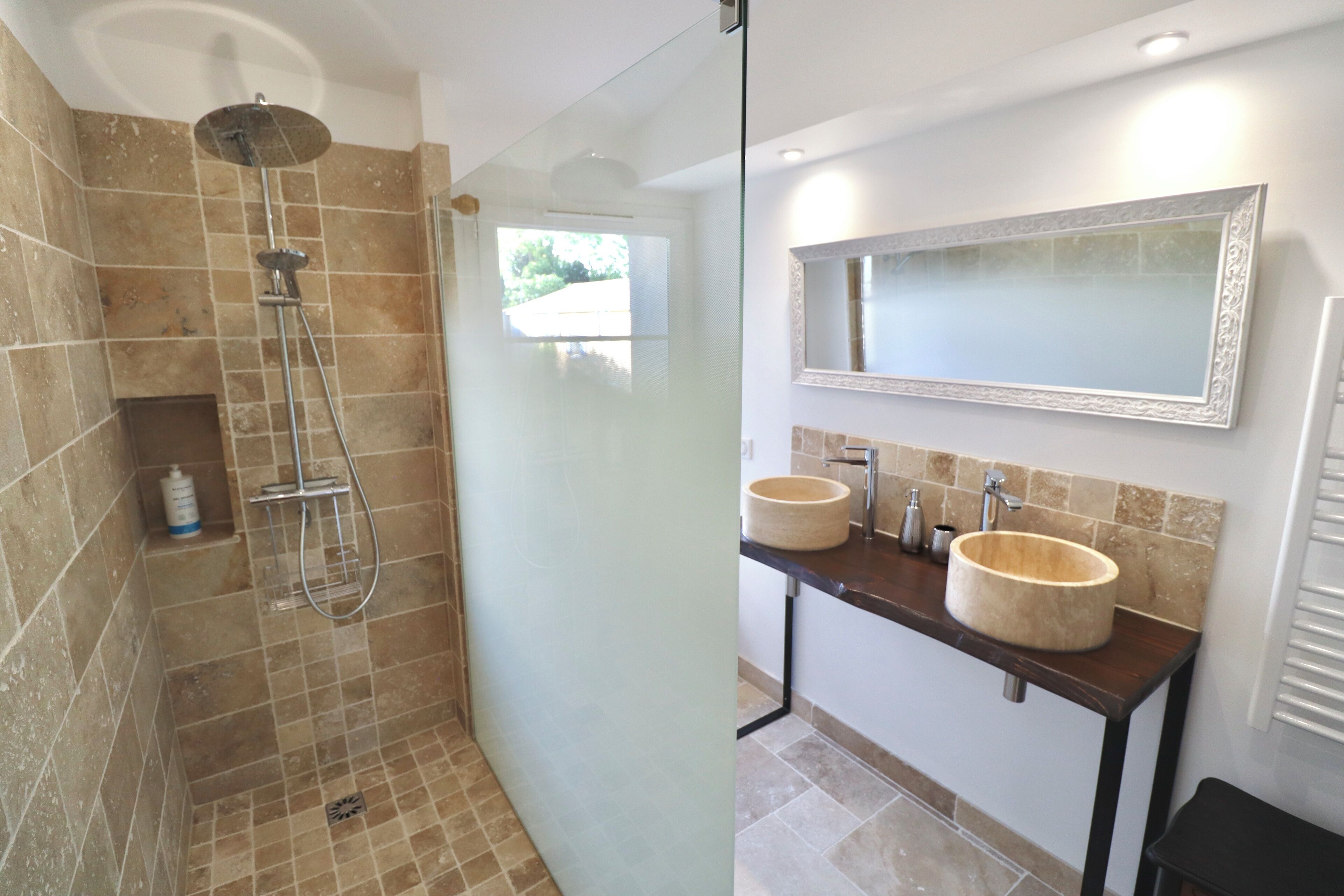 Ein Badezimmer mit einer gläsernen Dusche, zwei Waschbecken mit runden, beige farbenen Becken und einem großen Spiegel darüber.