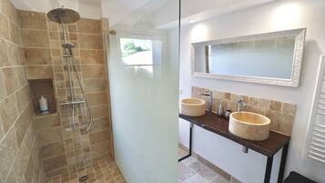 Ein Badezimmer mit einer gläsernen Dusche, zwei Waschbecken mit runden, beige farbenen Becken und einem großen Spiegel darüber.