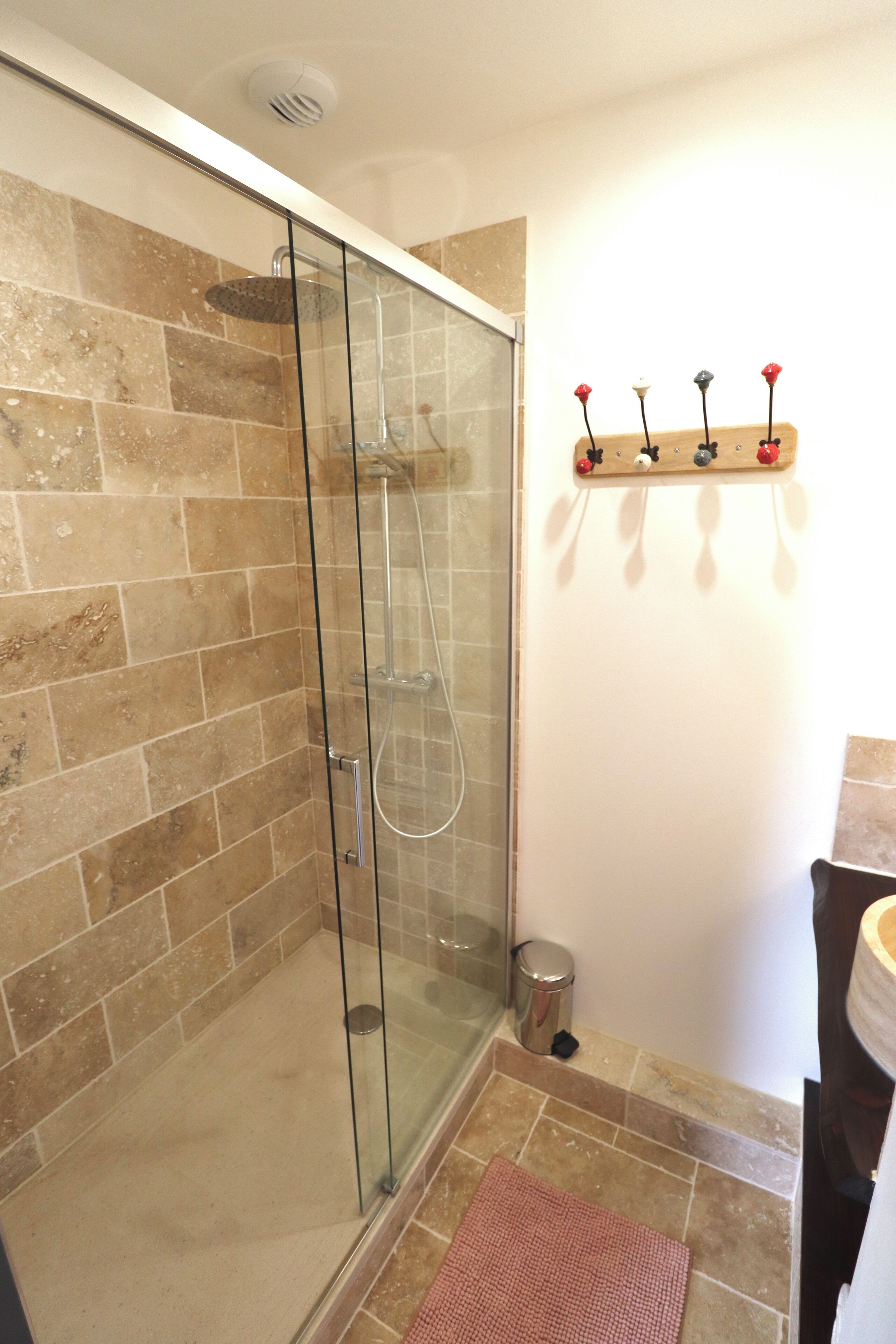 A shower with glass doors, a tiled wall, and a small trash can.