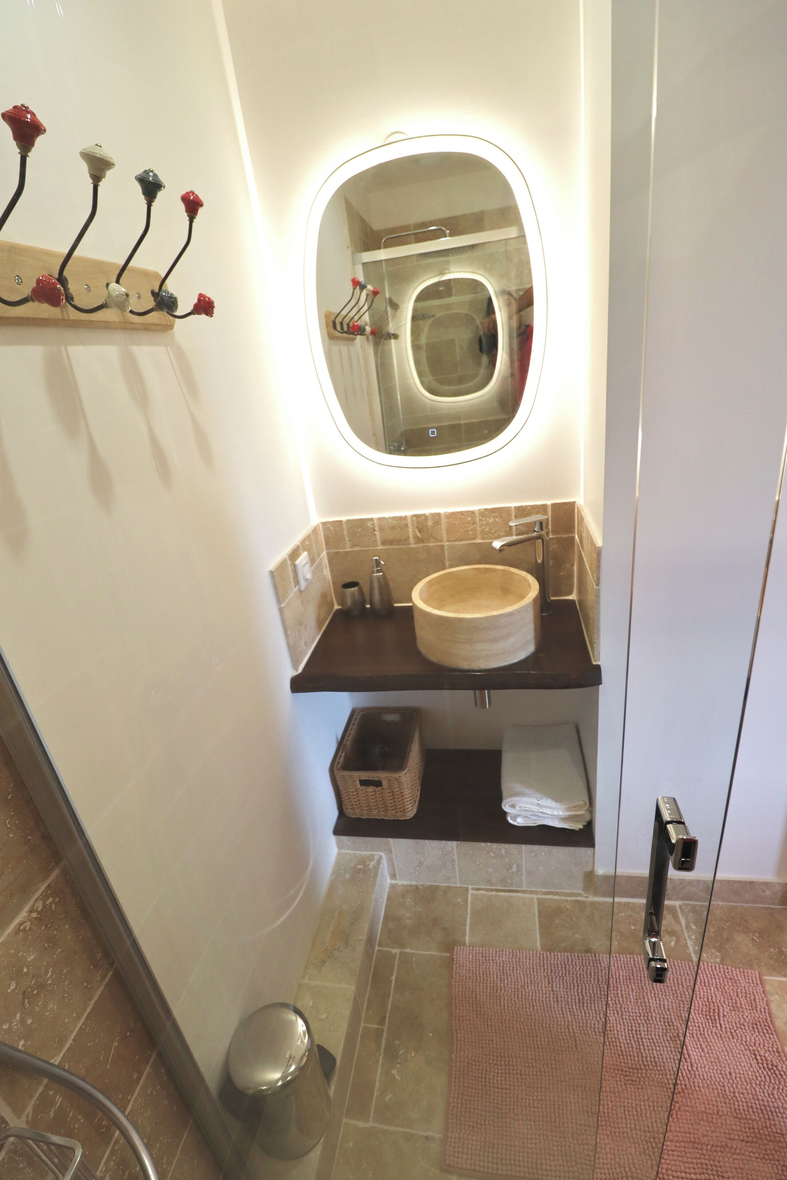 Un baño con un espejo redondo, un lavabo color crema y un perchero con flores decorativas.