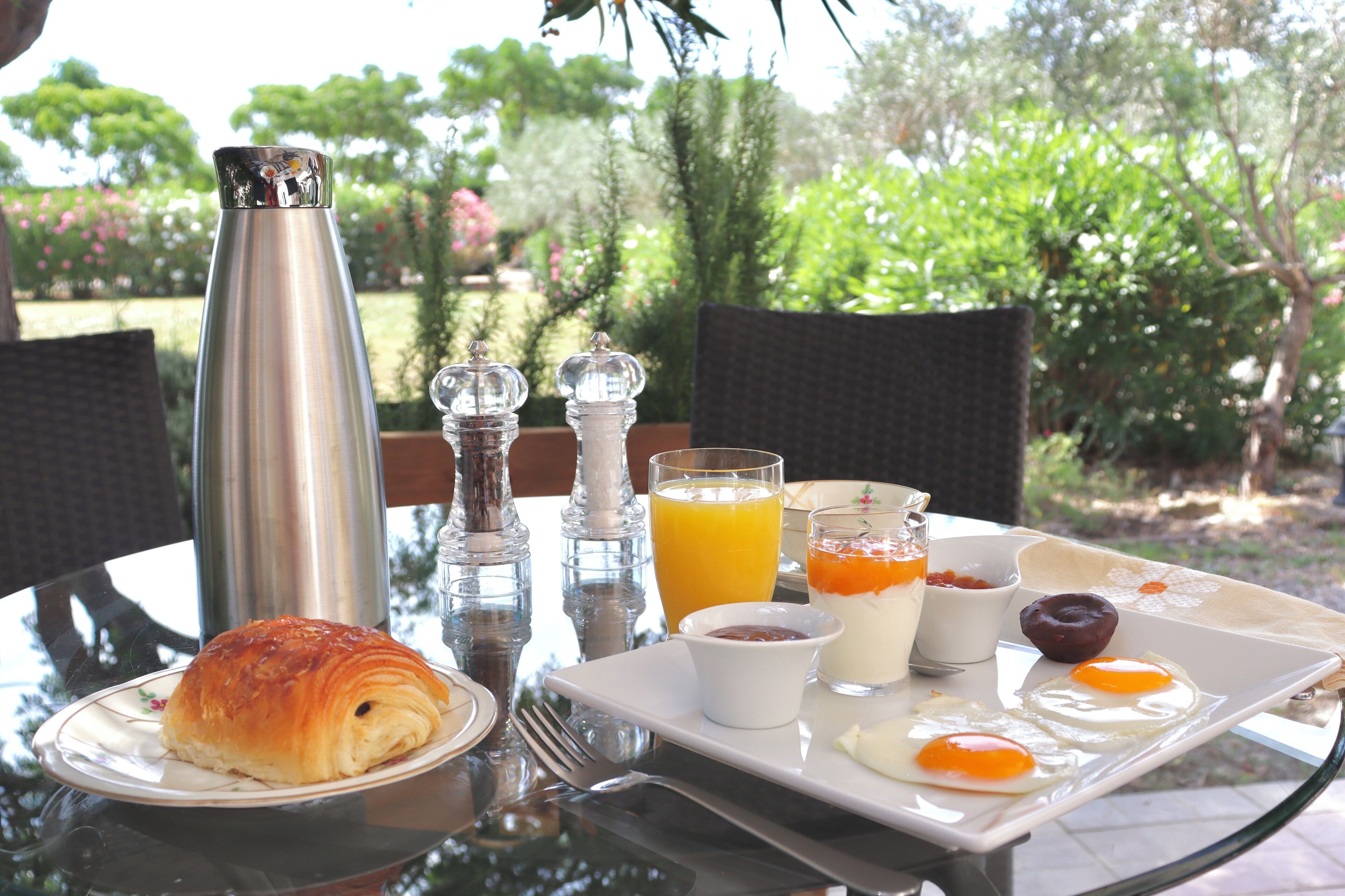Un plateau de petit-déjeuner avec des croissants, des œufs, du jus d’orange et de la confiture, posé sur une table à l’extérieur.