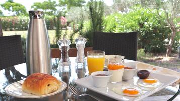 Un plateau de petit-déjeuner avec des croissants, des œufs, du jus d’orange et de la confiture, posé sur une table à l’extérieur.