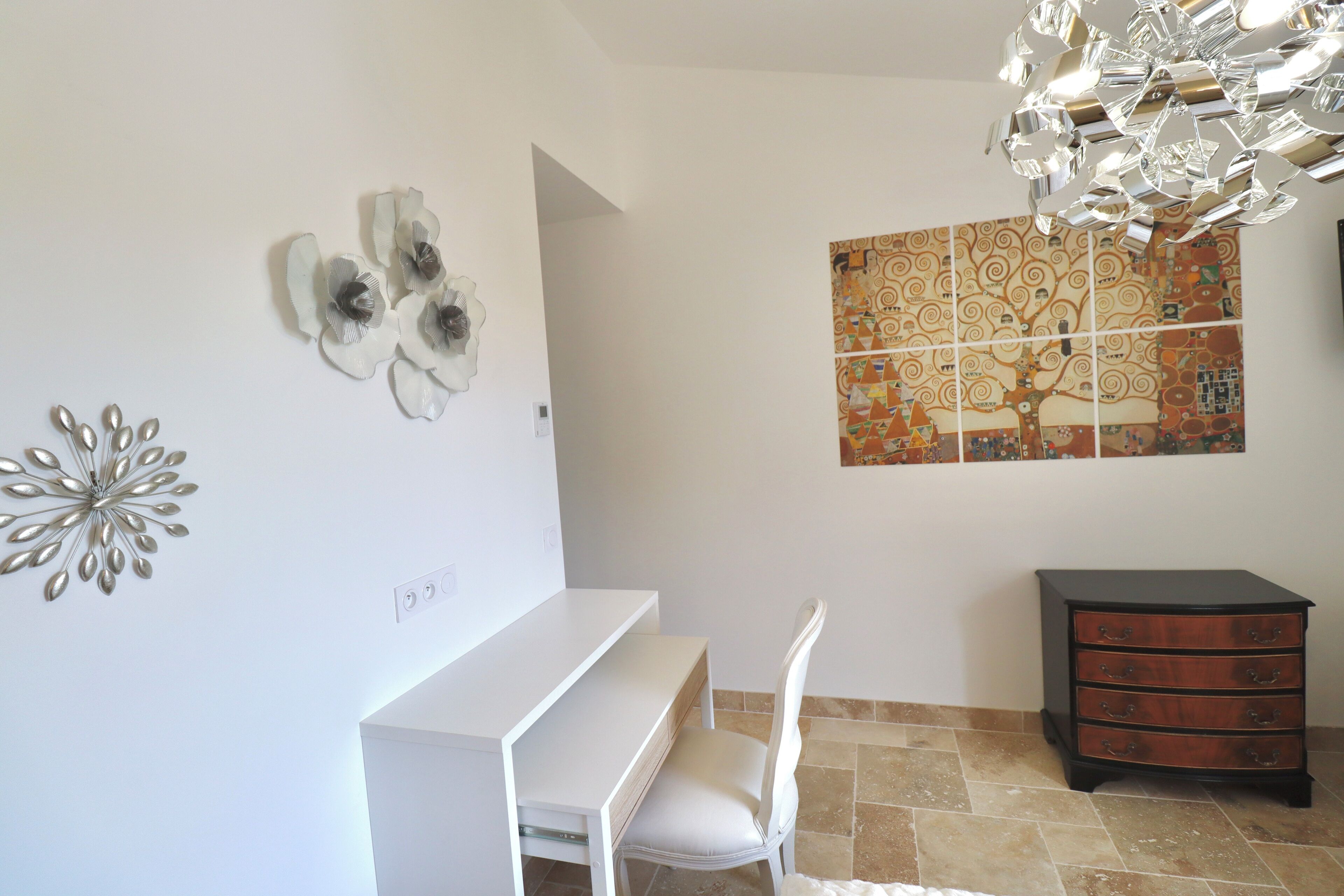 Una habitación con un escritorio blanco, una silla blanca, un aparador de madera y un adorno en la pared.