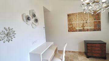 Una habitación con un escritorio blanco, una silla blanca, un aparador de madera y un adorno en la pared.